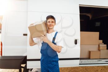 Deliveryman in uniform holds carton box at the car, delivery service. Man holding cardboard package, male deliver, courier or shipping job