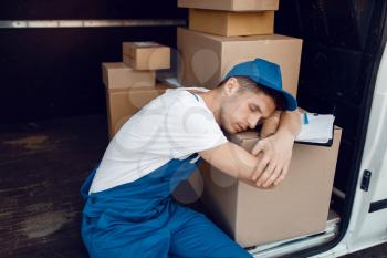 Tired loader in uniform sleeping on stack of parcels in the car, delivery service. Man standing at cardboard packages in vehicle, male deliver, courier or shipping job