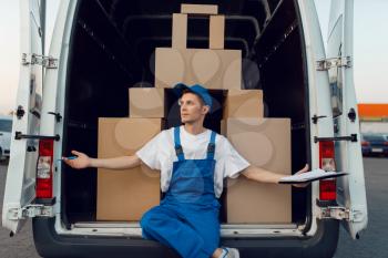 Deliveryman in uniform at the car, boxes are stacked in a pyramid shape, delivery service. Man standing at cardboard packages in vehicle, male deliver, courier or shipping job