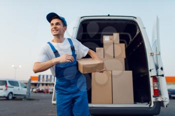 Deliveryman in uniform holds parcels at the car, delivery service, delivering. Man standing at cardboard packages in vehicle, male deliver, courier or shipping job
