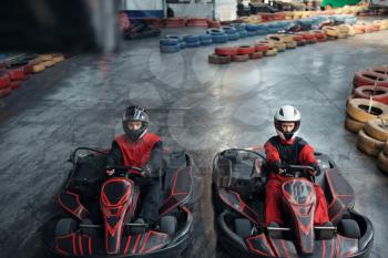 Two kart racers on start line, front view, karting auto sport indoor. Speed race on close go-cart track with tire barrier. Fast vehicle competition, high adrenaline leisure