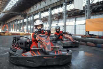 Two kart racers enters the turn, front view, karting auto sport indoor. Speed race on close go-cart track with tire barrier. Fast vehicle competition, high adrenaline leisure