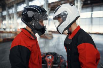 Two kart racers in helmets standing face to face, karting auto sport indoor. Speed race on close go-kart track with tire barrier. Fast vehicle competition, active hobby