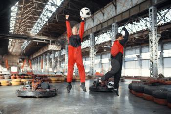 Two kart racers celebrates victory, karting auto sport indoor. Speed race on close go-kart track with tire barrier. Fast vehicle competition, active hobby