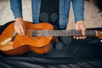 Male guitarist puts acoustic guitar in the case in music store. Assortment in musical instruments shop