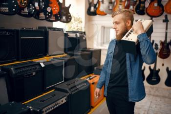 Young man choosing combo amplifier for electric guitar in music store. Assortment in musical instruments shop, male musician buying equipment