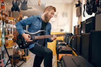 Male guitarist plays on electric guitar in music store. Assortment in musical instruments shop, musician buying equipment