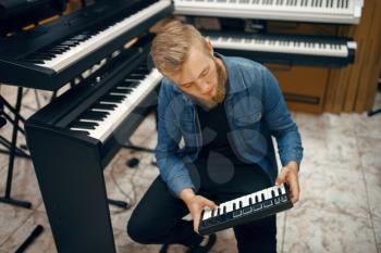 Bearded young musician buying synthesizer in music store. Assortment in musical instrument shop, male musician choosing keyboard