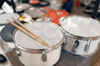 White drums and drumsticks on showcase in music store, closeup view, nobody. Assortment in musical instrument shop, professional equipment for musicians and performers