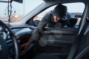 Car robber steals women's handbag, criminal lifestyle, stealing. Hooded male bandit opening vehicle on parking. Auto robbery