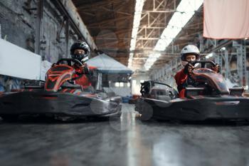 Two kart racers fight for victory on lap, side view, karting auto sport indoor. Speed race on close go-cart track with tire barrier. Fast vehicle competition