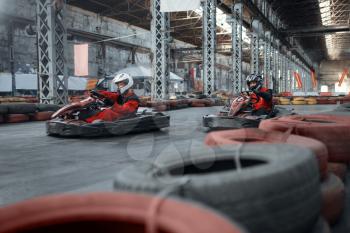 Two kart racers enters the turn, front view, karting auto sport indoor. Speed race on close go-cart track with tire barrier. Fast vehicle competition, high adrenaline leisure