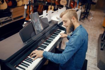 Male musician trying to play on piano in music store. Assortment in musical instruments shop, keyboardist buying equipment, pianist in market