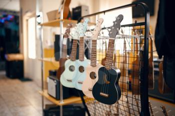 Row of ukulele acoustic guitars on showcase in music store, nobody. Assortment in musical instrument shop, professional equipment for musicians and performers