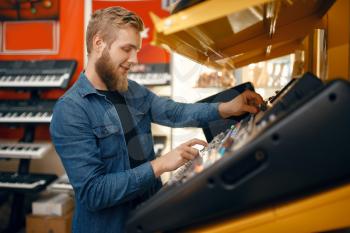 Bearded young man choosing synthesizer in music store. Assortment in musical instrument shop, male musician