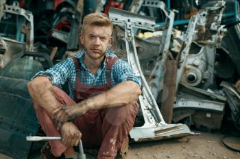 Dirty male repairman with wrench on car junkyard. Auto scrap, vehicle junk, automobile garbage, abandoned, damaged and crushed transport