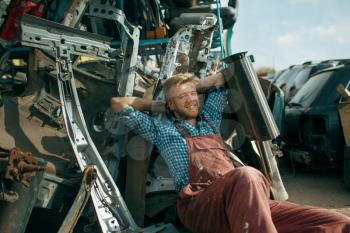 Male repairman relaxing on car junkyard at summer day. Auto scrap, vehicle junk, automobile garbage, abandoned, damaged and crushed transport