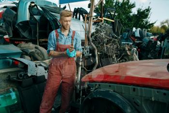Male repairman with towel on car junkyard. Auto scrap, vehicle junk, automobile garbage. Abandoned, damaged and crushed transport, scrapyard