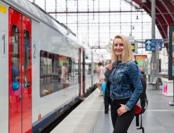 Female tourist with backpack waiting for train on railway station platform, travel in Europe. Transportation by european railroads, comfortable tourism and travelling