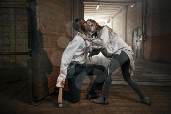 Female zombie attacked scaried man with axe in abandoned factory. Horror in city, creepy crawlies, doomsday apocalypse, bloody evil monsters