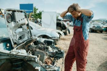 Angry male repairman works on car junkyard. Auto scrap, vehicle junk, automobile garbage, abandoned, damaged and crushed transport
