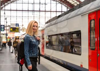 Female tourist with backpack waiting for train on railway station platform, travel in Europe. Transportation by european railroads, comfortable tourism