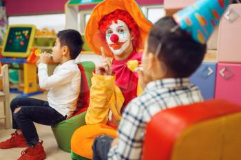 Funny clown play with cheerful children together. Birthday party celebrating in playroom, baby holiday in playground. Childhood happiness, childish leisure