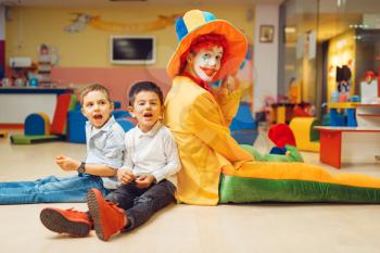Funny clown animator play with boys in kindergarten. Birthday celebrating in playroom, baby holiday in playground. Childhood happiness, childish leisure, entertainment in children's area