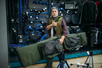 Male angler holds big case for fishing-rods in fishing shop. Equipment and tools for fish catching and hunting, accessory choice on showcase in store