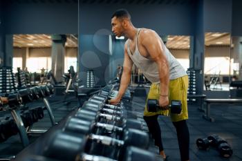 Muscular man choosing heavy dumbbells on training in gym. Fitness workout in sport club, healthy lifestyle, fit exercise