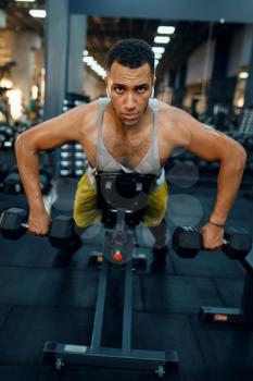 Muscular man in sportswear doing exercise with dumbbells on the bench, training in gym. Workout in sport club, healthy lifestyle