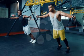 Two muscular athletes in sportswear at stretching exercise machine on training in gym. Workout in sport club, healthy lifestyle