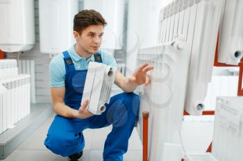 Plumber in uniform shows water heating radiator in plumbering store. Man buying sanitary engineering in shop