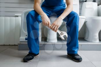 Plumber in uniform sitting on toilet at the showcase in plumbering store. Man buying sanitary engineering tools and equipment in shop
