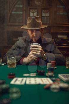 Poker player in suit and hat plays in casino, risk addiction. Games of chance. Man leisures in gambling house, gaming table with green cloth