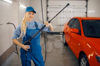 Female washer in uniform poses with high pressure gun in hands, car wash service. Woman cleans vehicle, carwash station, car-wash business