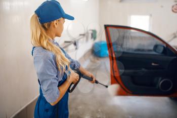 Female washer in uniform cleans door with high pressure gun in hands, car wash. Woman washes vehicle, carwash station, car-wash business