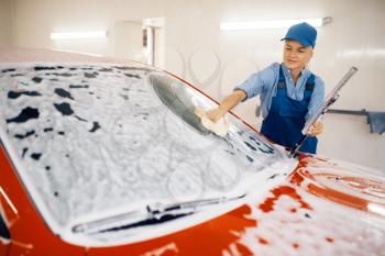 Female washer with sponge wipes the automobile windshield, car wash. Woman cleans vehicle, a carwash station