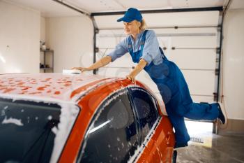 Female washer with sponge wipes the automobile windshield, car wash. Woman cleans vehicle, a carwash station