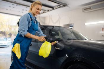 Female washer with wax spray cleans automobile, waxing on car wash service. Woman washes vehicle, carwash station, car wash business