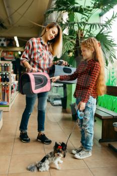 Mother with daughter choosing bag for little dog in pet store. Woman and little child buying equipment in petshop, accessories for domestic animals