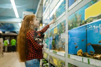 Little girl with puppy looking on fishes in aquarium, pet store. Child buying equipment in petshop, accessories for domestic animals