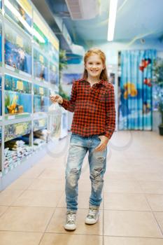 Happy little girl looking on goldfish in pet store. Child buying equipment in petshop