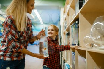 Mother with daughter choosing aquarium in pet store. Woman and little child buying equipment in petshop, accessories for domestic animals