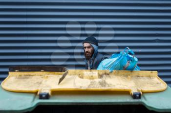 Bearded poor searching food in trashcan on city street. Poverty is a social problem, homelessness and loneliness, alcoholism and drunk addiction, urban lonely