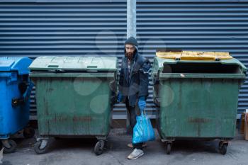 Bearded bum searching food in trashcan on city street. Poverty is a social problem, homelessness and loneliness, alcoholism and drunk addiction, urban lonely