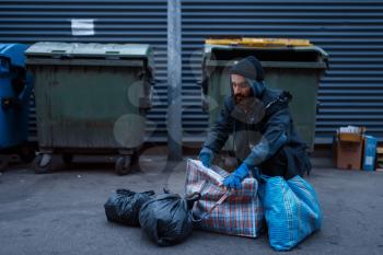 Bearded dirty poor at the trashcan on city street. Poverty is a social problem, homelessness and loneliness, alcoholism and drunk addiction, urban lonely