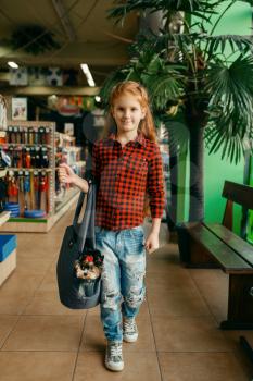 Little girl with her puppy in bag, pet store. Child buying equipment in petshop, accessories for domestic animals