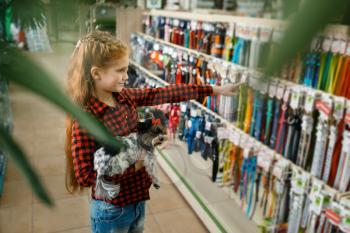 Little girl choosing leash and collar for her puppy, pet store. Child buying equipment in petshop, accessories for domestic animals
