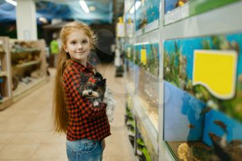 Little girl with puppy looking on fishes in aquarium, pet store. Child buying equipment in petshop